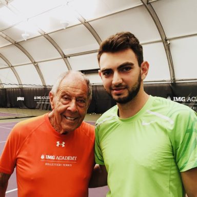 Zwei Männer auf einem Tennisplatz; älterer Mann in orange, jüngerer in grünem Shirt.