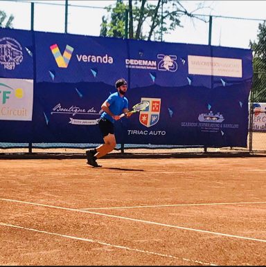 Mann in blauer Sportkleidung spielt Tennis auf einem Sandplatz.