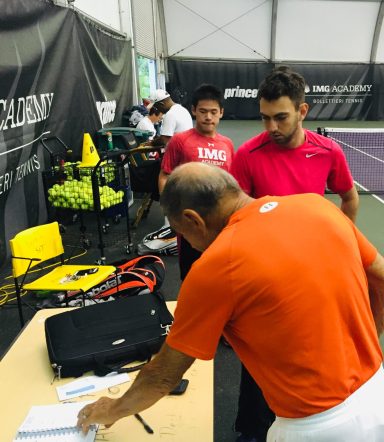 Zwei Männer in Sportkleidung diskutieren am Tisch in einer Tennis-Halle.