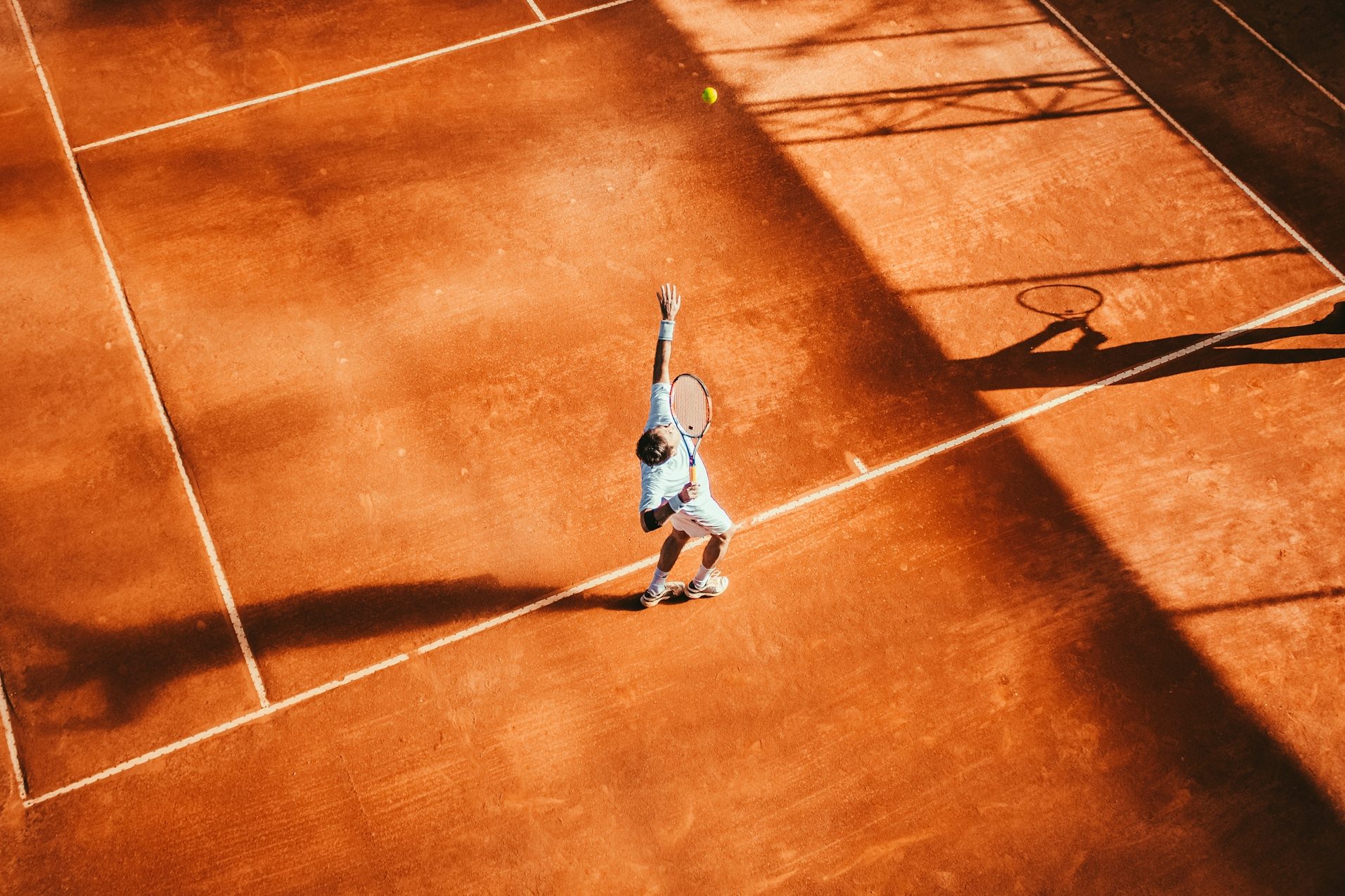 Tennisspieler beim Aufschlag auf einem roten Sandplatz.