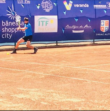 Junger Tennisspieler in Aktion auf einem Sandplatz, mit blauem Shirt und schwarzer Hose.