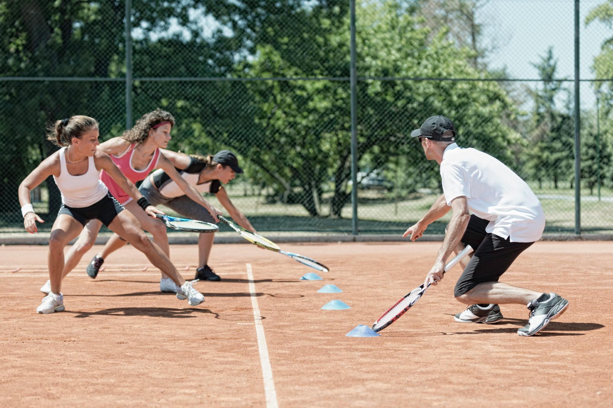 Vier Personen spielen Tennis auf einem Sandplatz und üben mit Schlägern.