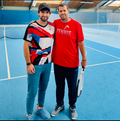 Zwei Männer auf einem Tennisplatz, einer trägt ein buntes T-Shirt, der andere ein rotes.