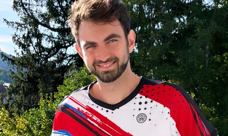 Junger Mann mit Bart in einem gestreiften Sporttrikot vor einer natürlichen Kulisse.